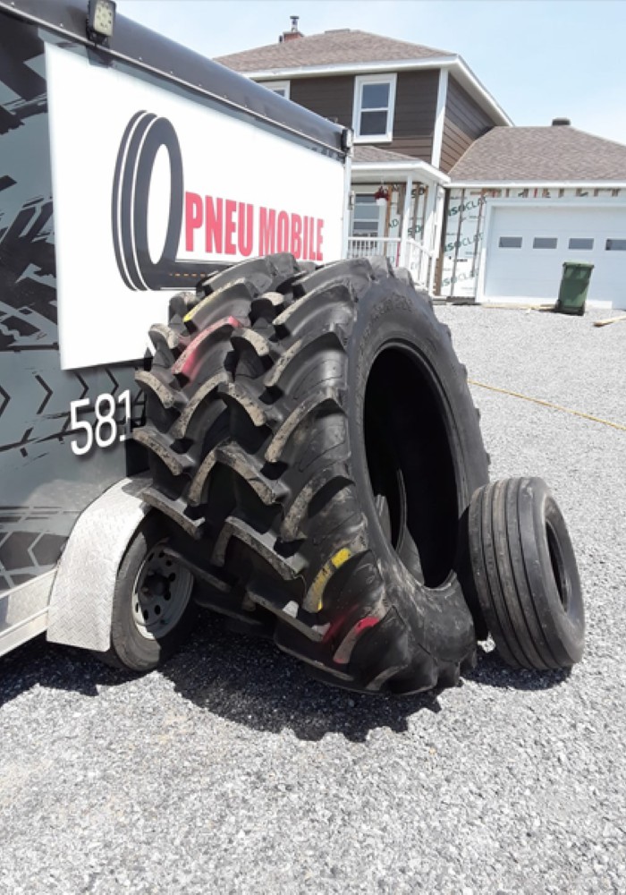 Deux pneus agricoles, l’un de grande taille et l’autre plus petit, posés contre la remorque de Pneu Mobile Rive-Sud.